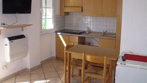 A compact kitchen with wooden cabinets, a built-in microwave, a sink, and a television mounted on the wall.