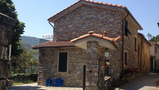 A stone building with a tiled roof, a small porch, and a gravel driveway.