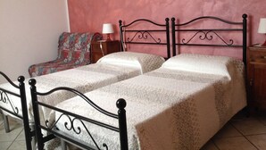 A room with two beds, a chair, a nightstand, and a lamp.