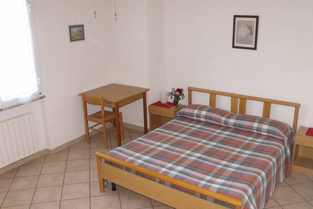 Un dormitorio con una cama de madera, una mesita pequeña de madera, una mesita de noche, una ventana y un radiador.