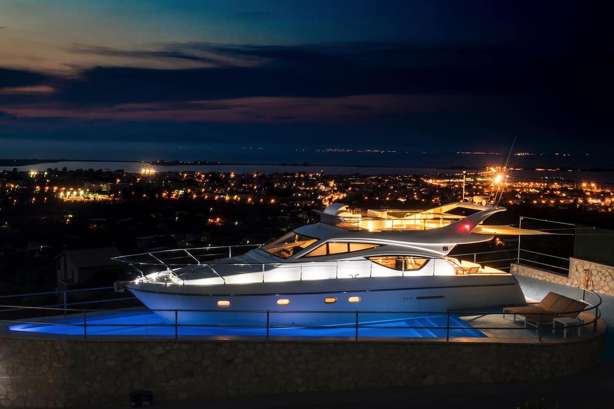 A yacht docked at a waterfront property with a pool and a view of a cityscape at night.