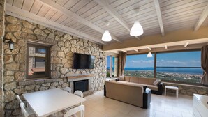 Una habitación con paredes de piedra, una chimenea, un sofá, una mesa de comedor y un televisor.