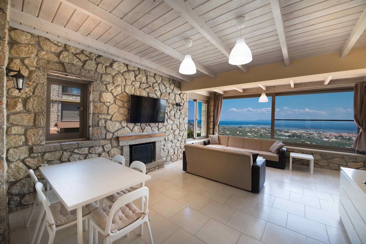 A stone-walled room with a fireplace, a sofa, a dining table, and a TV.