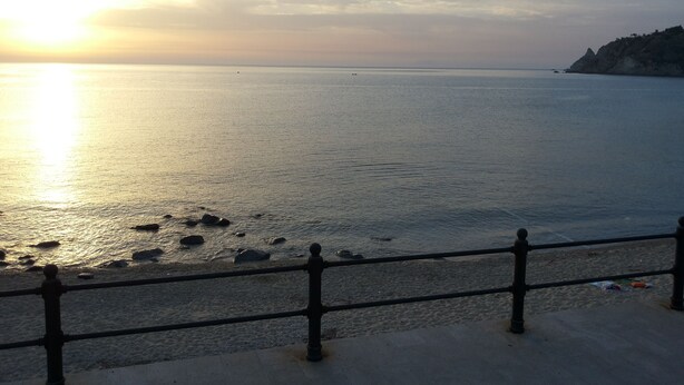 A coastal view with a metal railing in the foreground, a calm sea, and a distant rocky coastline under a clear sky. - B&B Il Nido (Ricadi)