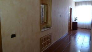 A hallway with a tiled floor, a door with a mirror, and a small plant on a stand. - B&B Il Nido (Ricadi)