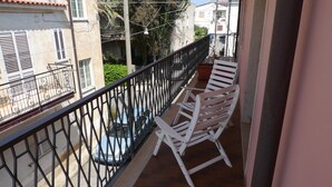 A balcony with a metal railing, two white chairs, and a blue car parked on the street below. - B&B Il Nido (Ricadi)