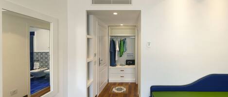 A narrow hallway with a wooden floor, a mirrored closet door, and a bed with a green and blue bedspread.