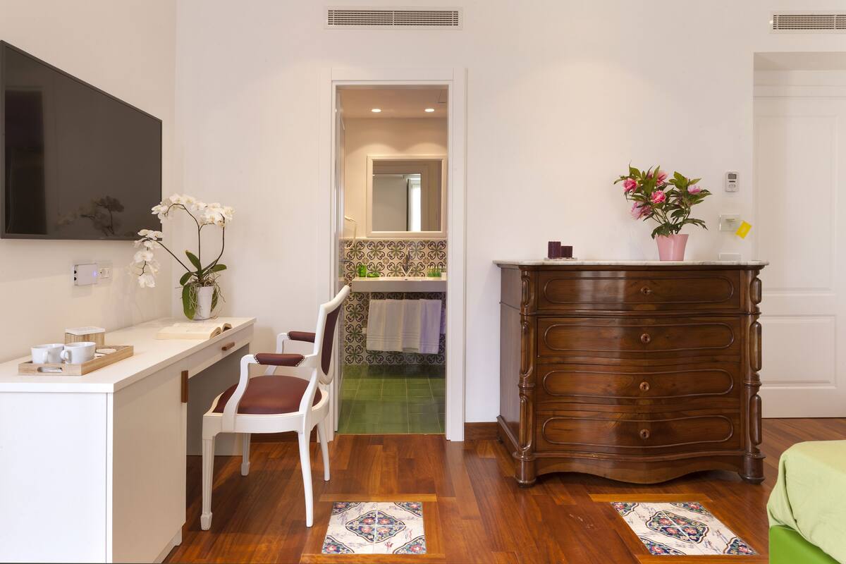Une pièce comprenant une commode en bois, un bureau blanc, une chaise, un miroir et une plante en pot.