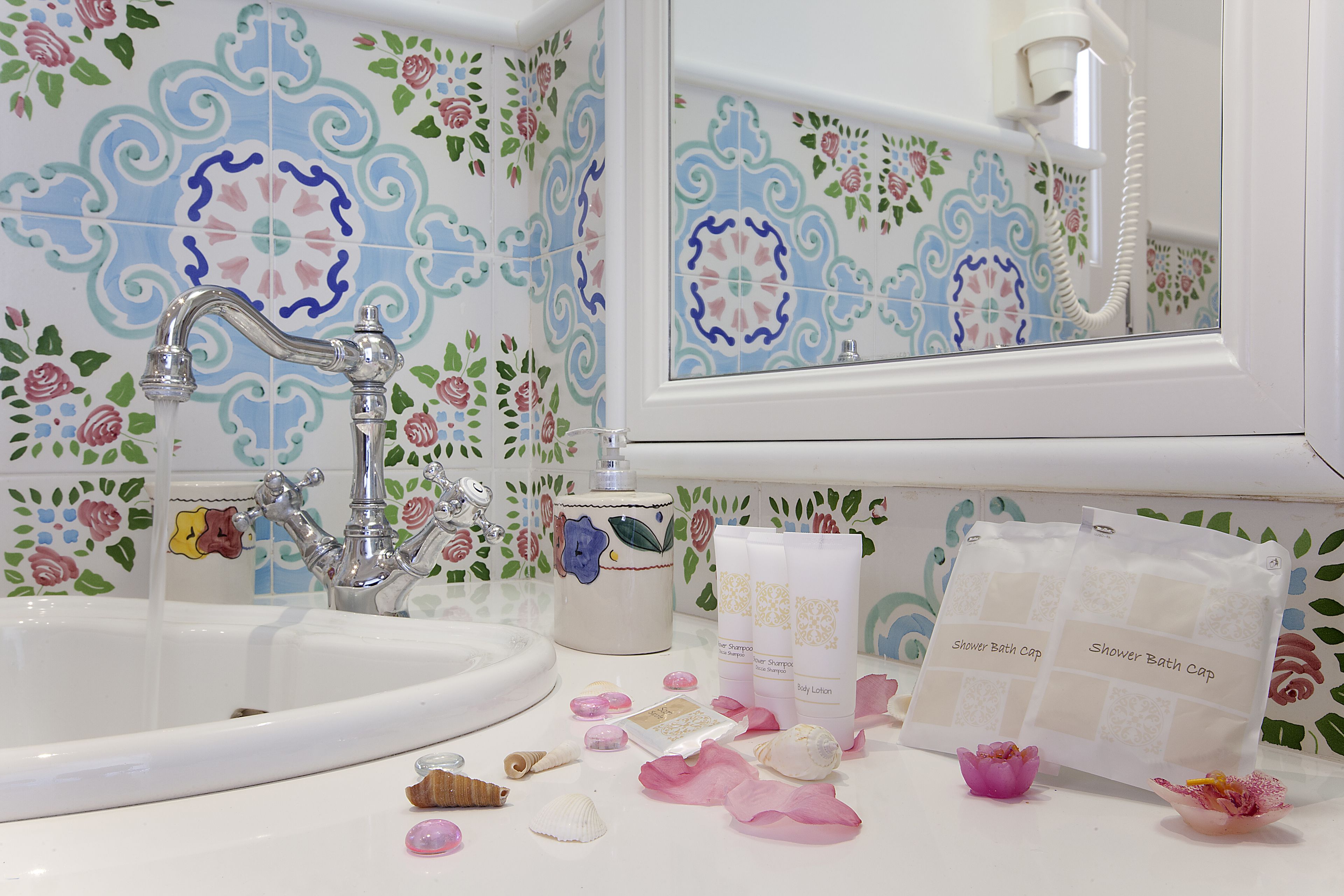 Un baño con lavamanos blanco, un espejo y una ducha. Hay artículos de aseo en la encimera.