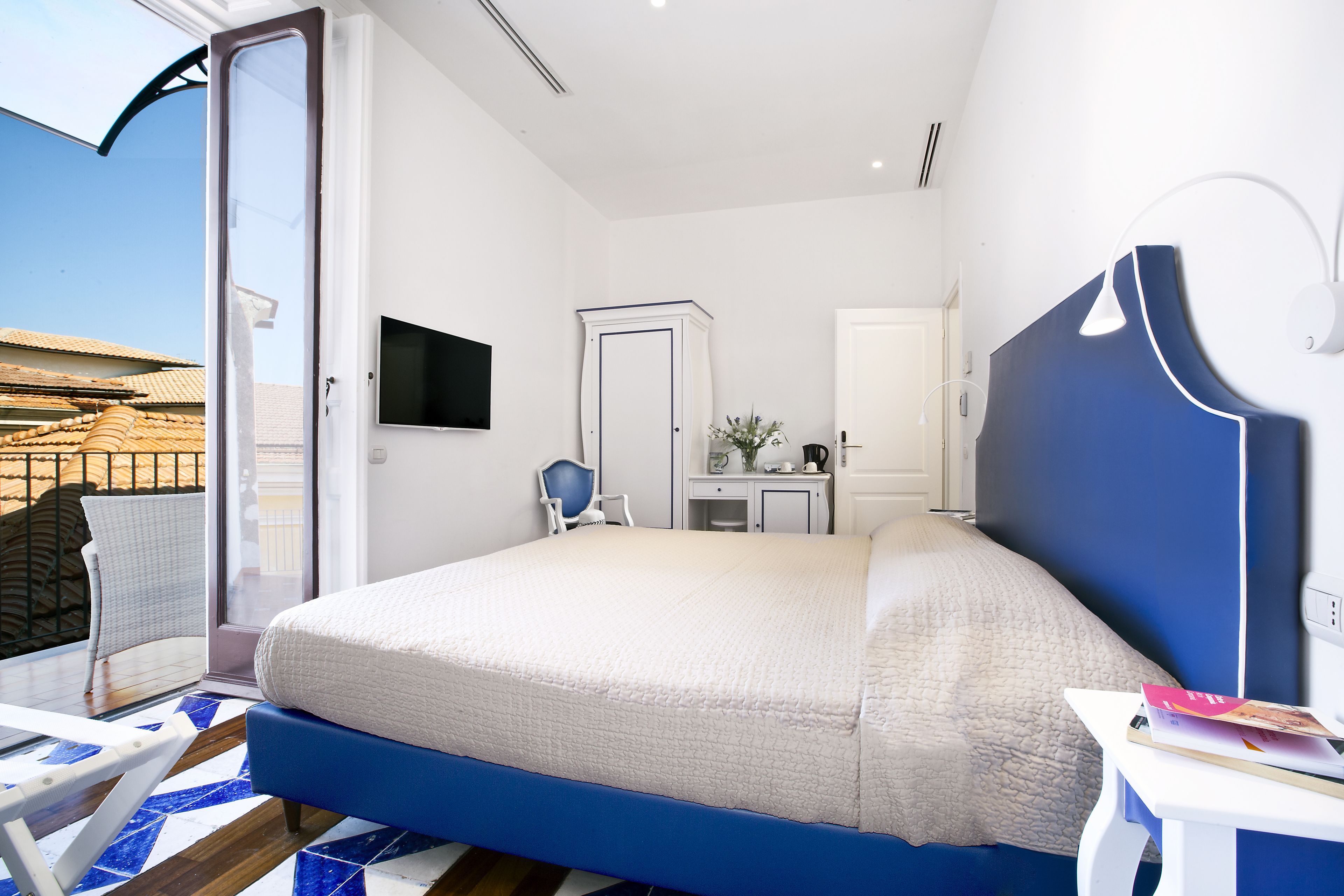 A bedroom with a large bed, a desk, a chair, and a TV on the wall.