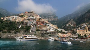 Une ville côtière avec des bâtiments construits sur une colline, des bateaux amarrés dans le port et des montagnes en arrière-plan.