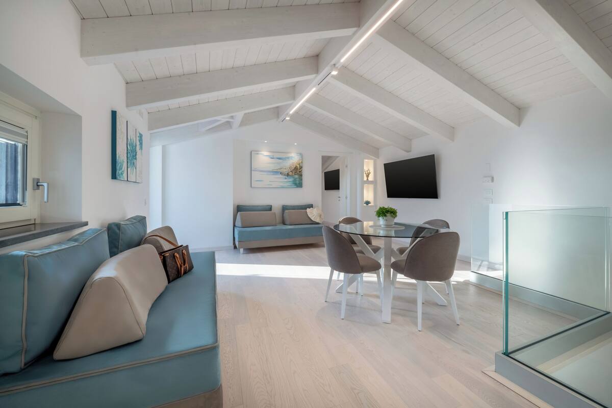 Un salon moderne avec un canapé bleu, une table à manger en verre entourée de chaises, et un coin cuisine à l’arrière-plan.