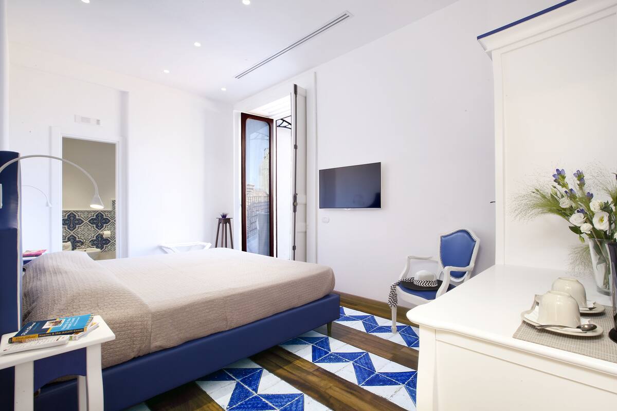 Une chambre d’hôtel moderne équipée d’un lit, d’une table de chevet, d’une chaise, d’une télévision et offrant une vue sur la ville par la fenêtre.