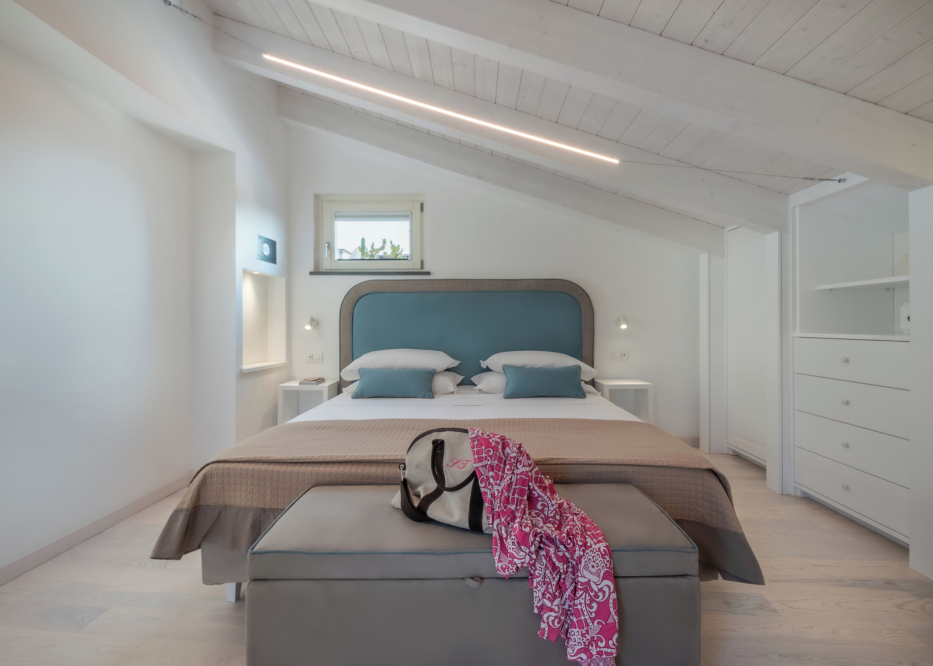 A modern bedroom with a large bed, bedside tables, a wardrobe, and a window with a view.