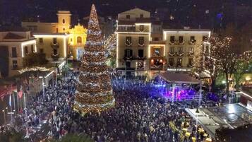Una folla numerosa si è riunita attorno a un abete decorato in una piazza, con edifici sullo sfondo.