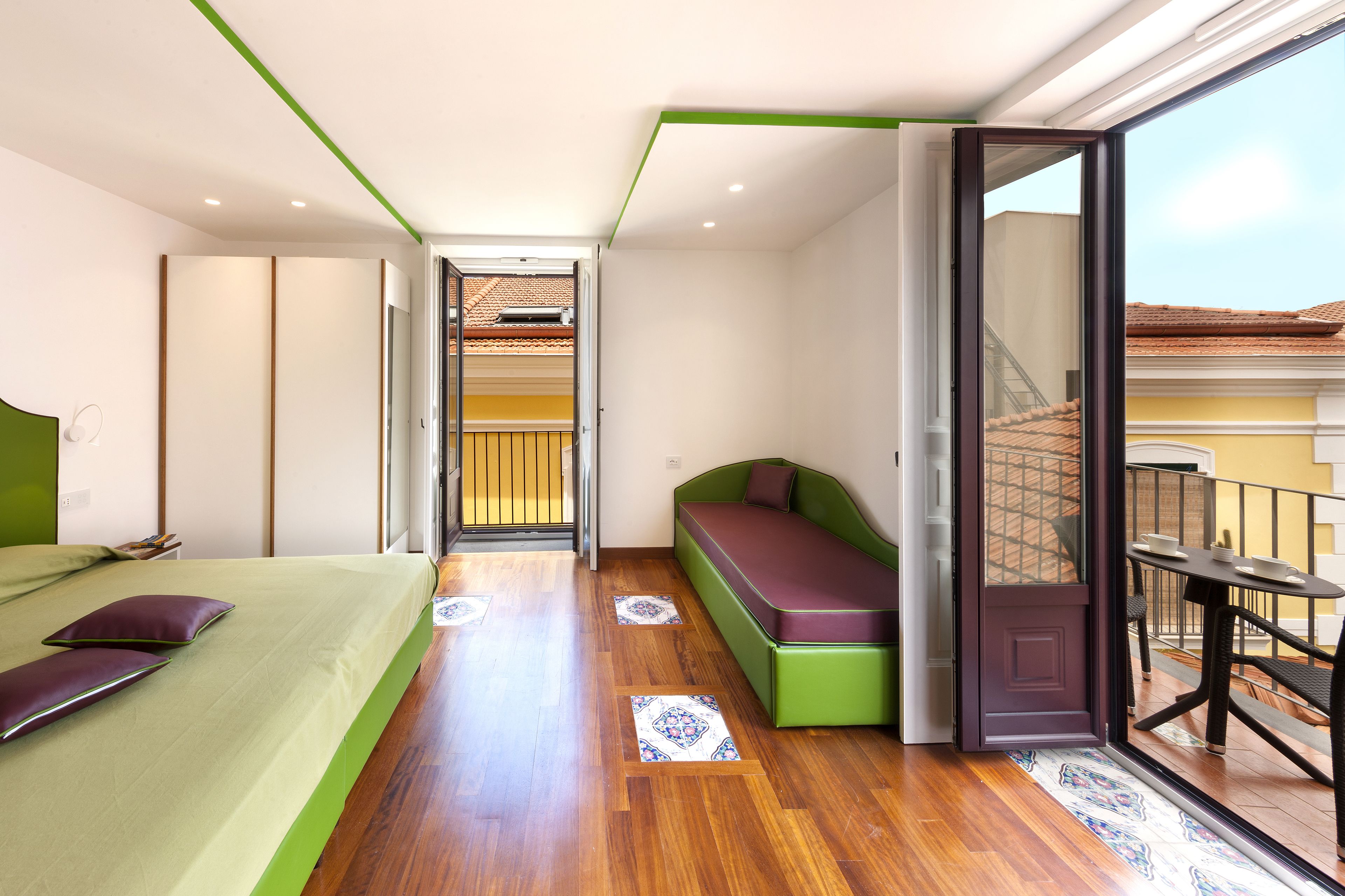 A modern bedroom with a bed, a bench, and a balcony with a table and chairs.