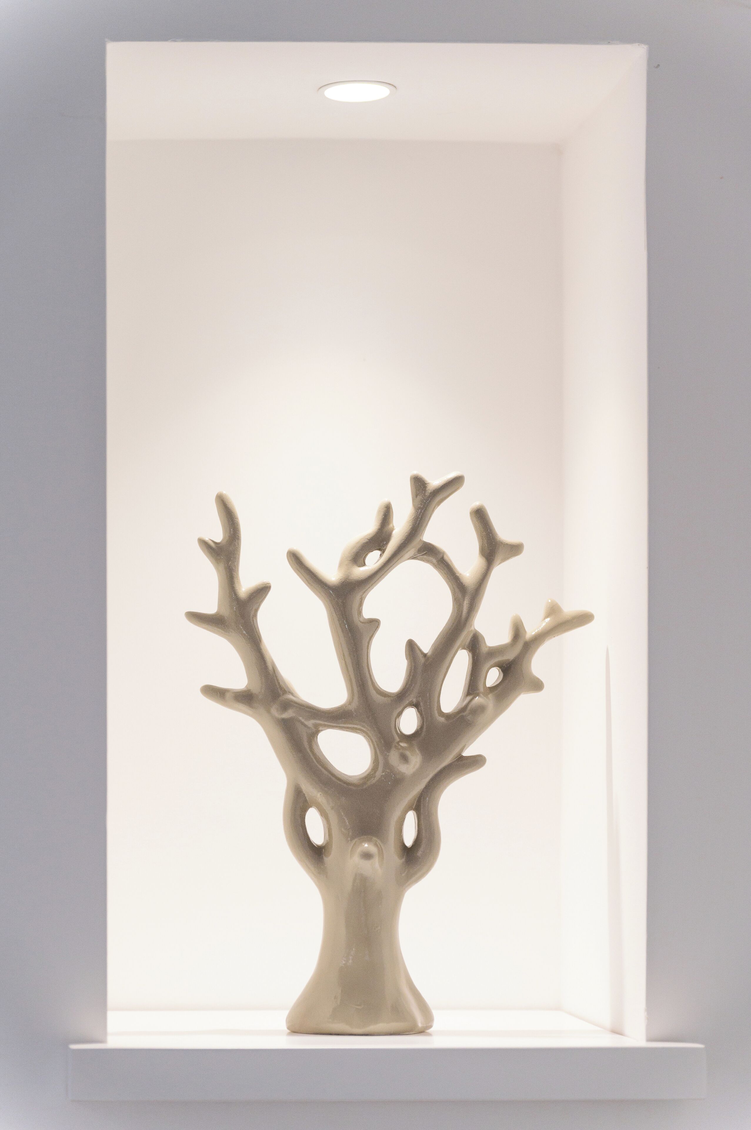 Una escultura abstracta de un árbol blanco en una habitación blanca con una luz empotrada en el techo.