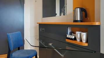 Una cucina moderna con un tavolo in vetro, una sedia blu, un bollitore e una macchina da caffè.