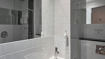 A modern bathroom with a glass-enclosed shower, a sink with a mirror, and a wall-mounted soap dispenser.