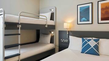 A hotel room with bunk beds, a bedside table with a lamp, and framed pictures on the wall.