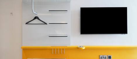 Una habitación moderna con un mueble blanco y amarillo, un televisor de pantalla plana y una pequeña mesa con cubierta de vidrio.