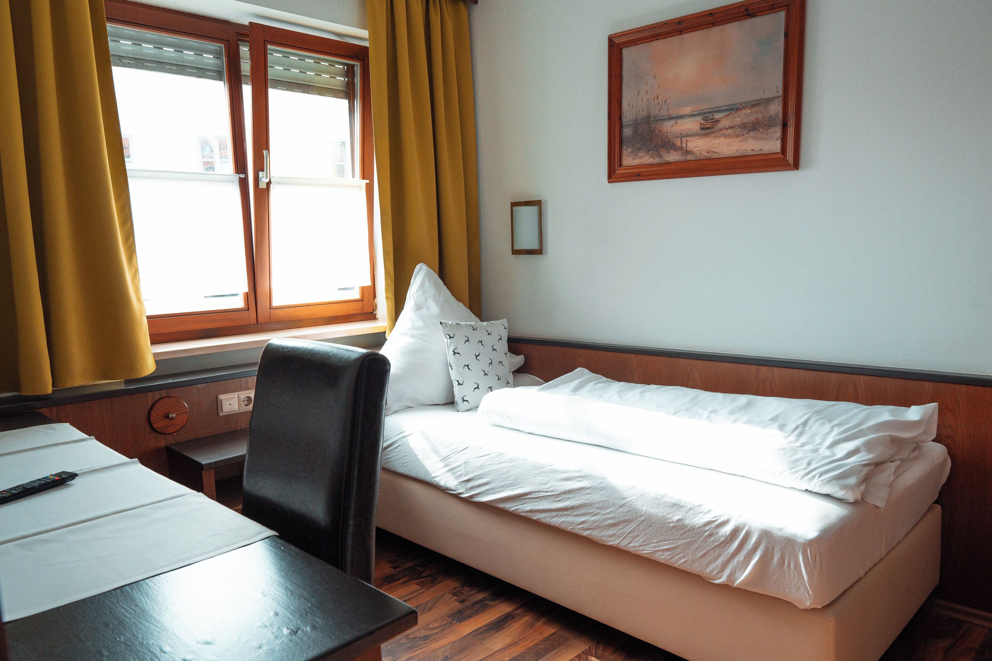 Habitación de hotel con cama, escritorio, silla, ventana con cortinas amarillas y un cuadro en la pared.