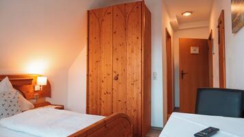 A hotel room with a wooden wardrobe, a bed with white bedding, a nightstand with a lamp, and a table with a remote control.
