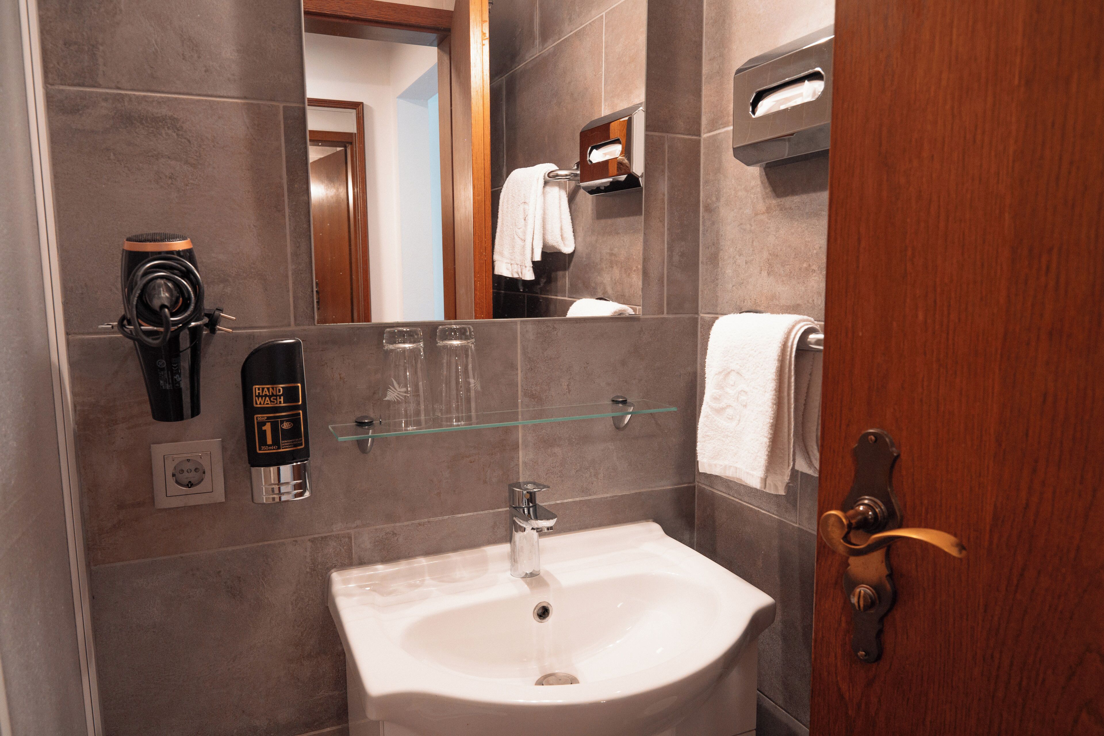 Ein Badezimmer mit Waschbecken, Handseifen-Spender, Seifenschale aus Glas und Handtuchhalter.