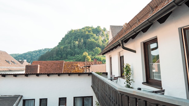 Un edificio residencial con balcón, una ventana con vista a una colina boscosa y una chimenea de ladrillo.