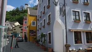Una calle adoquinada con un edificio amarillo, un edificio blanco con cajas de flores y un letrero de restaurante.