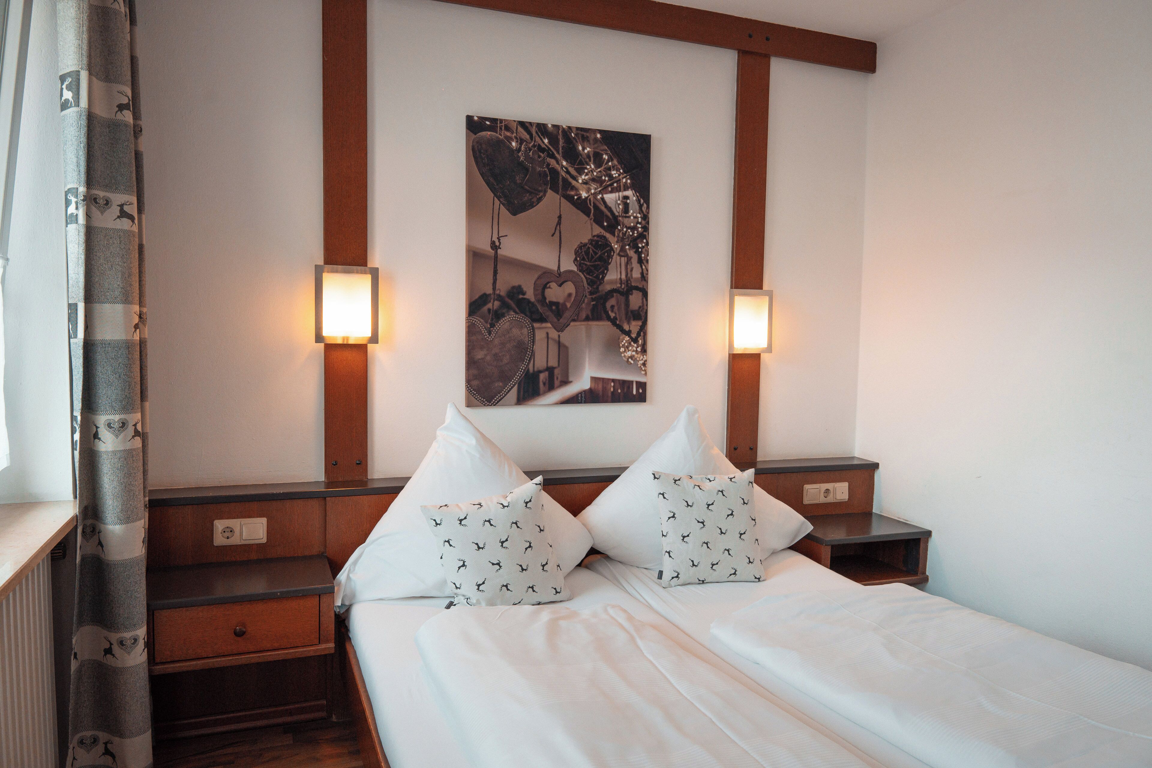 A hotel room with a bed, two nightstands, a wall-mounted light fixture, and a curtain.