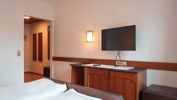 Ein Hotelzimmer mit einem Bett, einer Holzkommode, einem flachbildfernseher an der Wand und einem kleinen Schreibtisch mit Lampe.