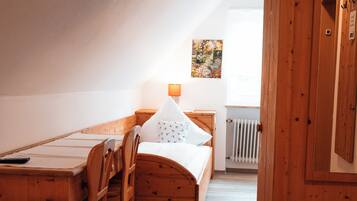 Een houten bed met een wit kussen en een klein tafeltje met een lamp.