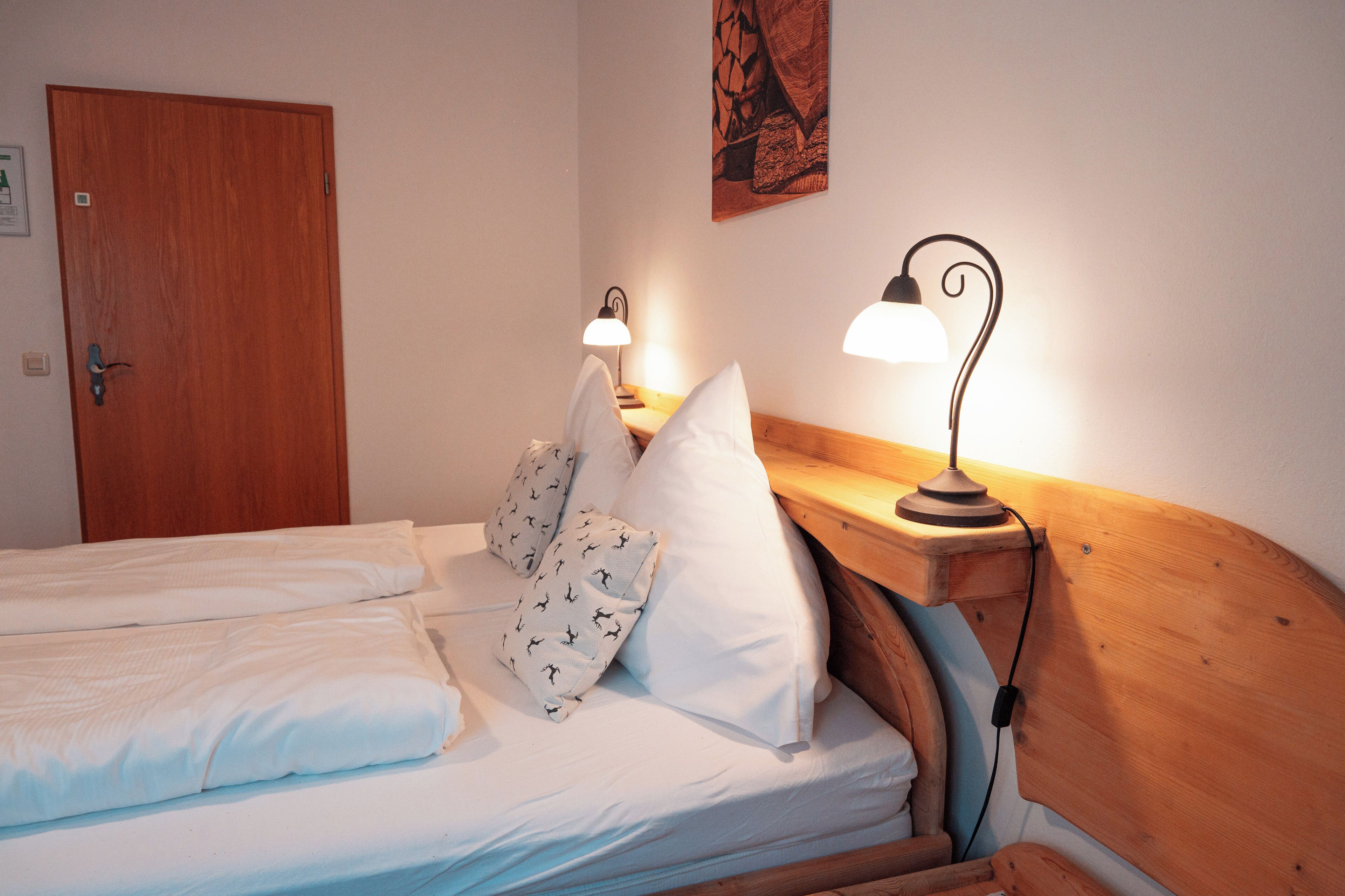 A hotel room with a wooden headboard, a bed with white linens, two bedside lamps, and a door.