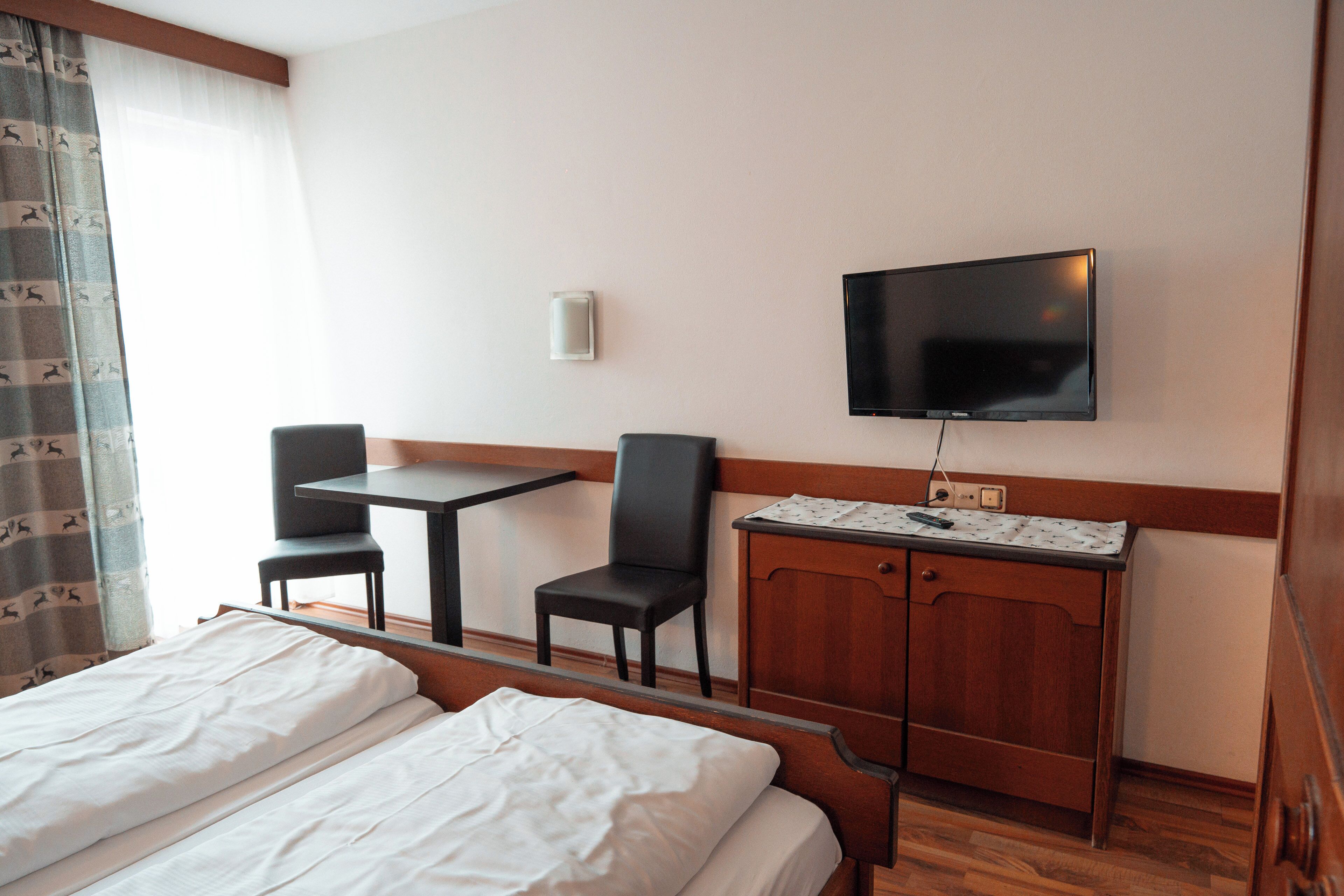Een hotelkamer met een bed, twee stoelen, een tafeltje, een televisie en een houten kast.