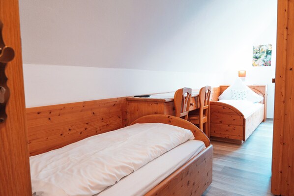 Una cama de madera con colchón blanco y una mesita de noche de madera con una lámpara.