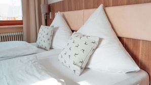 Una cama bien tendida con sábanas blancas y almohadas estampadas, cabecera de madera y lámpara de noche.