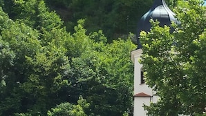 Una estructura que parece un castillo, con una torre destacada y un edificio más pequeño con una cruz en la parte superior, rodeados de abundante vegetación.
