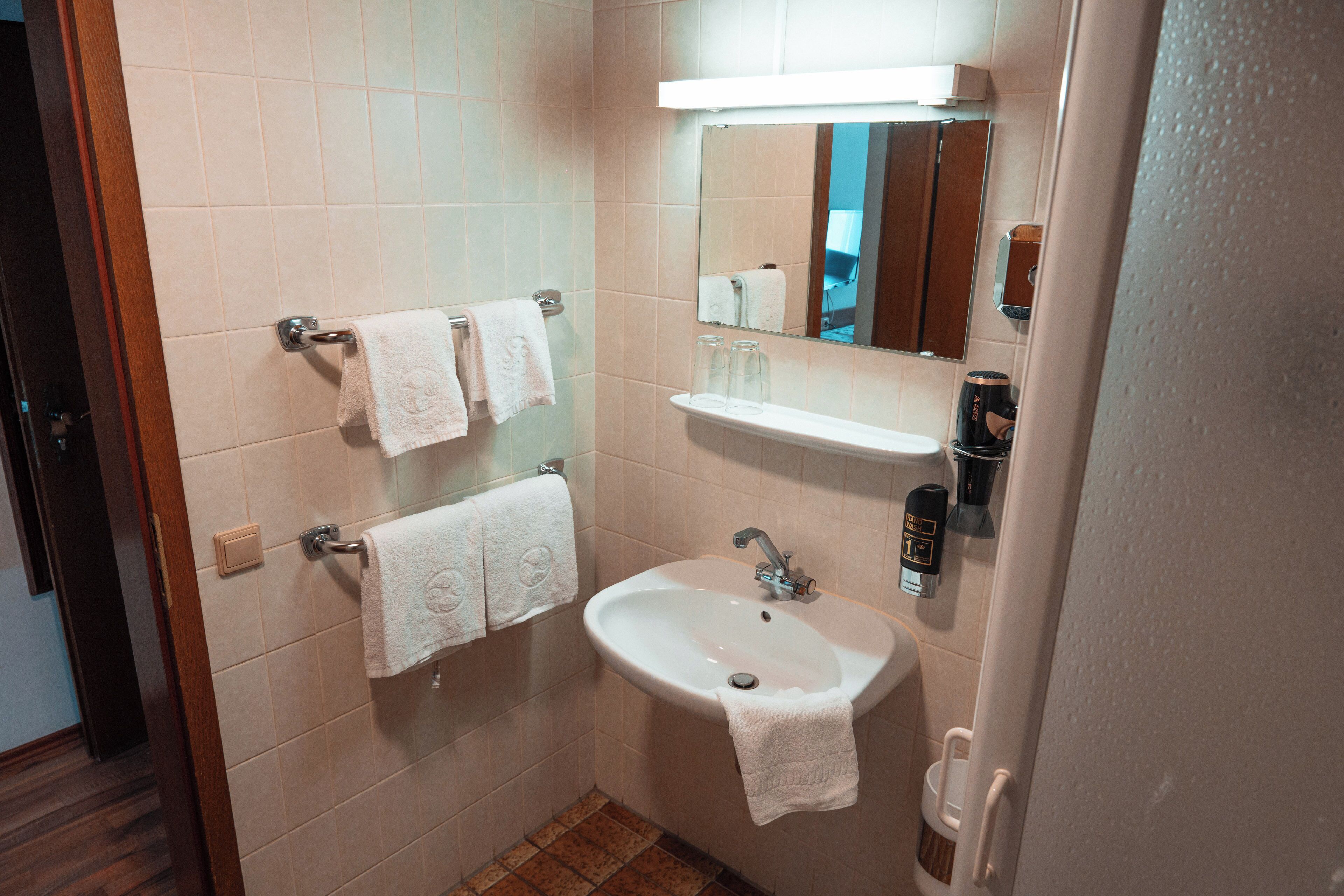 Un baño con lavamanos, espejo, toallero y un pequeño estante.