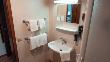 Un baño con lavamanos, espejo, toallero y un pequeño estante.