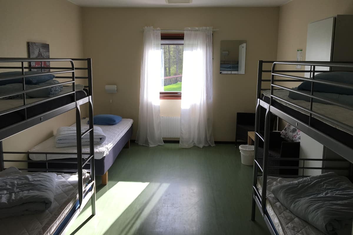 Une chambre de dortoir avec des lits superposés, une fenêtre avec des rideaux, un radiateur et une petite table avec une chaise.