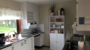 A kitchen with white cabinets, a stove, a sink, and a window with a view of greenery.