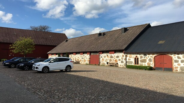 A stone building with a red door, parked cars, and a cobblestone driveway.
