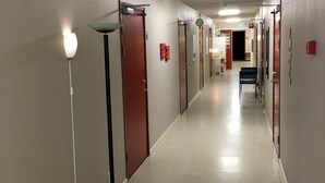 A long, narrow hallway with doors on both sides, a bench, and a floor lamp.
