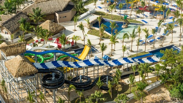 Ett semesterparadis med en vattenpark, palmer och byggnader med halmtak.