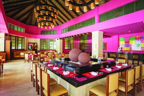 A spacious restaurant with a central bar area, multiple dining tables, and a vibrant color scheme. - Grand Memories Punta Cana All Inclusive (Punta Cana)