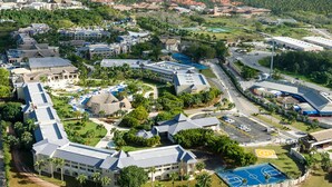 Ett flygbildsbild av ett semesterområde med flera byggnader, en swimmingpool och en tennisbana.