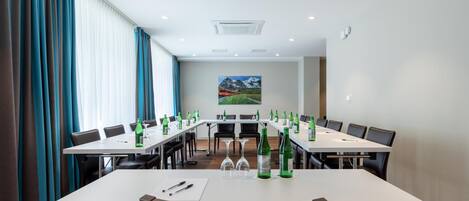 A conference room with long tables, chairs, and green bottles on each table.