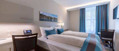 A hotel room with a bed, a desk, a chair, a telephone, and a painting on the wall.