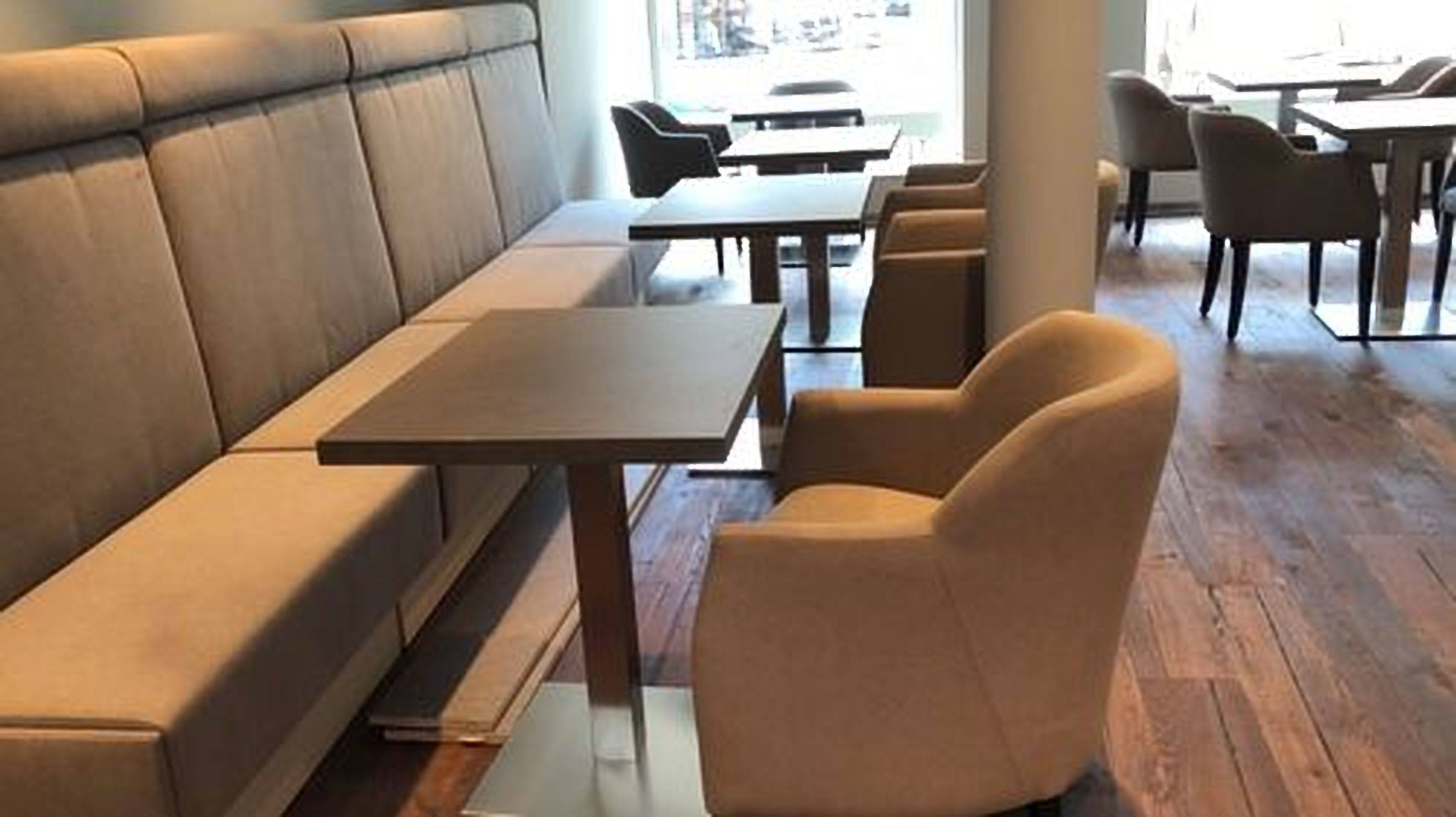 Ein modernes Restaurant mit einer langen Sitzbank, einzelnen Tischen und Holzboden.